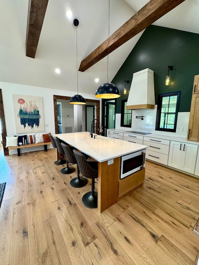 kitchen with a sink, stainless steel microwave, black electric stovetop, light wood-style flooring, and custom range hood