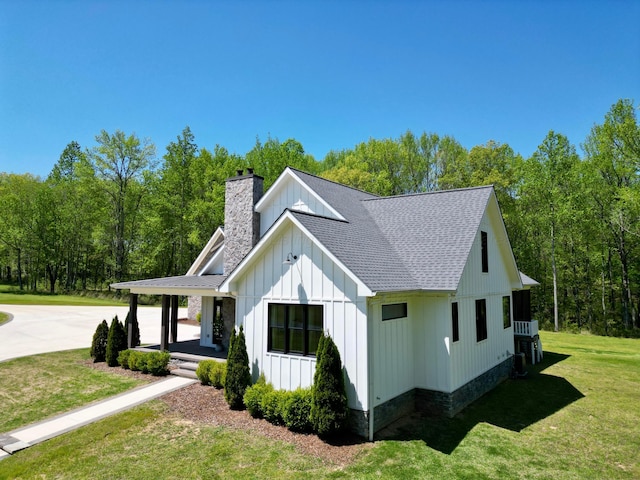 view of side of property with a chimney, central AC unit, board and batten siding, a lawn, and roof with shingles
