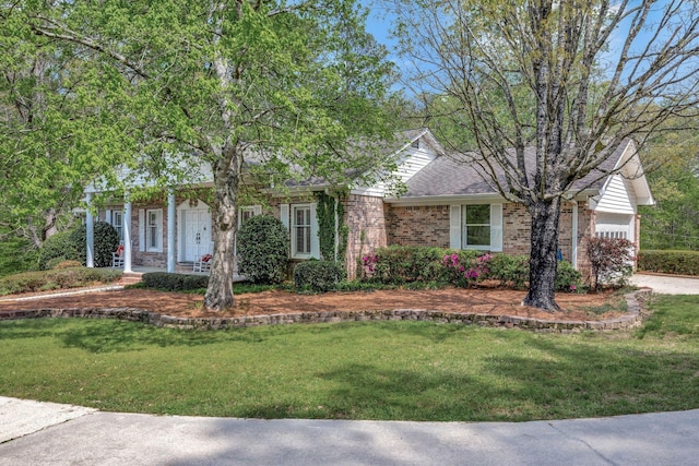 view of front of property featuring brick siding, roof with shingles, a front yard, and covered porch