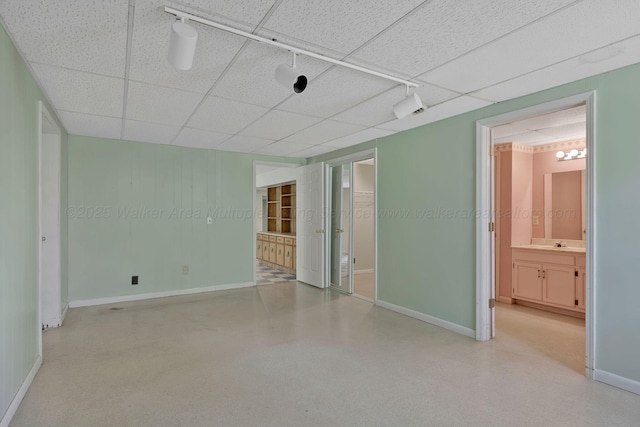 unfurnished room featuring rail lighting, a drop ceiling, and baseboards