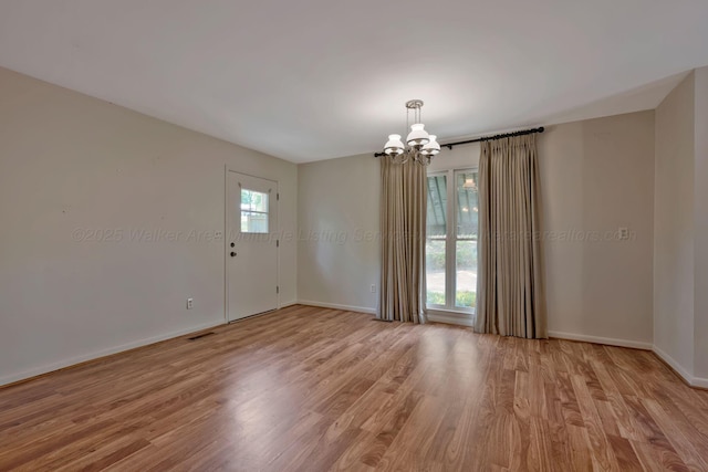 spare room with a chandelier, light wood-type flooring, visible vents, and baseboards