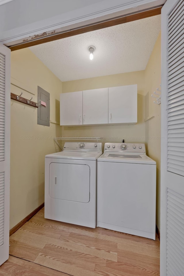 laundry area featuring electric panel, light wood-style flooring, a textured ceiling, independent washer and dryer, and cabinet space