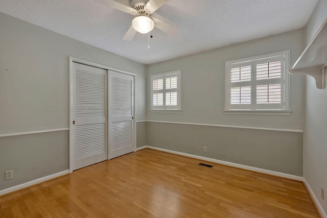 unfurnished bedroom featuring a textured ceiling, baseboards, visible vents, wood finished floors, and a closet