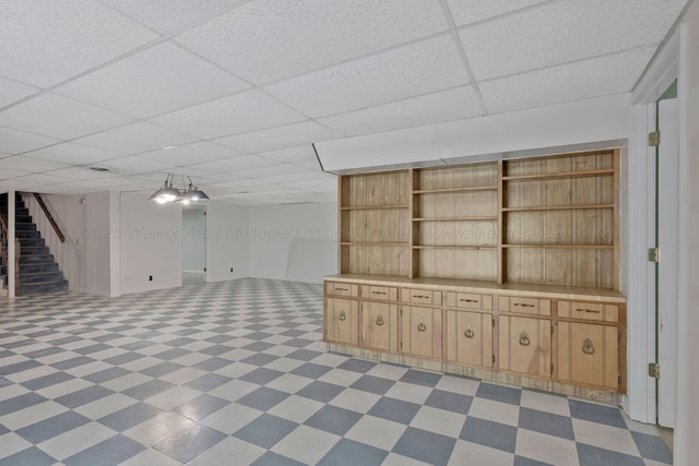 finished below grade area featuring light floors, stairs, and a paneled ceiling
