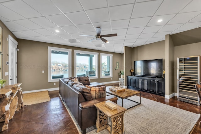 living room featuring baseboards, recessed lighting, a ceiling fan, a drop ceiling, and beverage cooler
