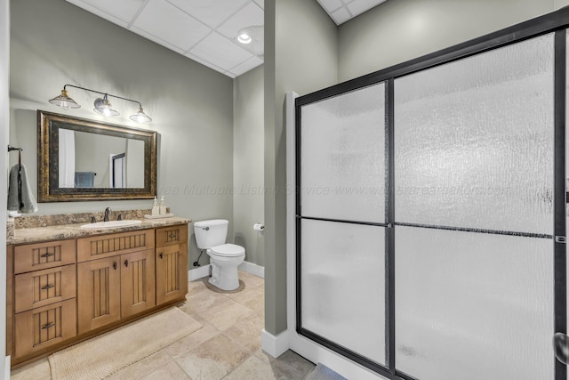 bathroom featuring toilet, vanity, a shower stall, baseboards, and a paneled ceiling