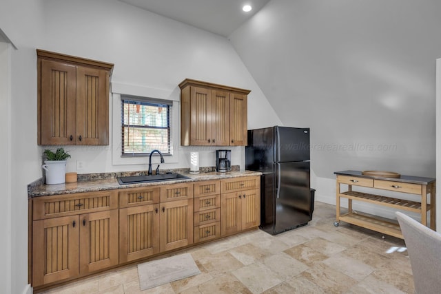 kitchen with lofted ceiling, recessed lighting, dark stone countertops, a sink, and freestanding refrigerator