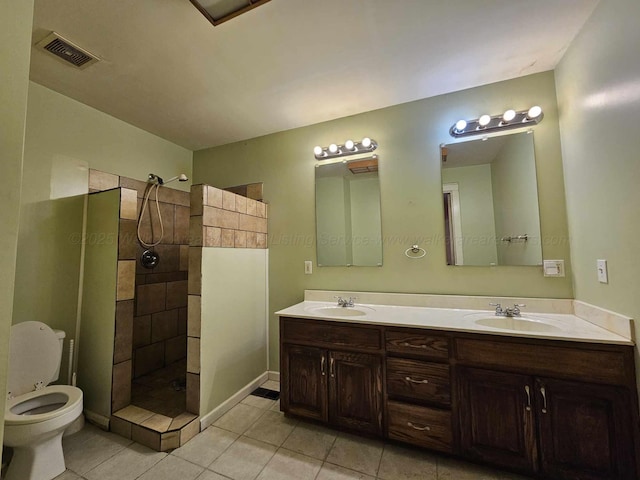 bathroom with tile patterned flooring, vanity, tiled shower, and toilet