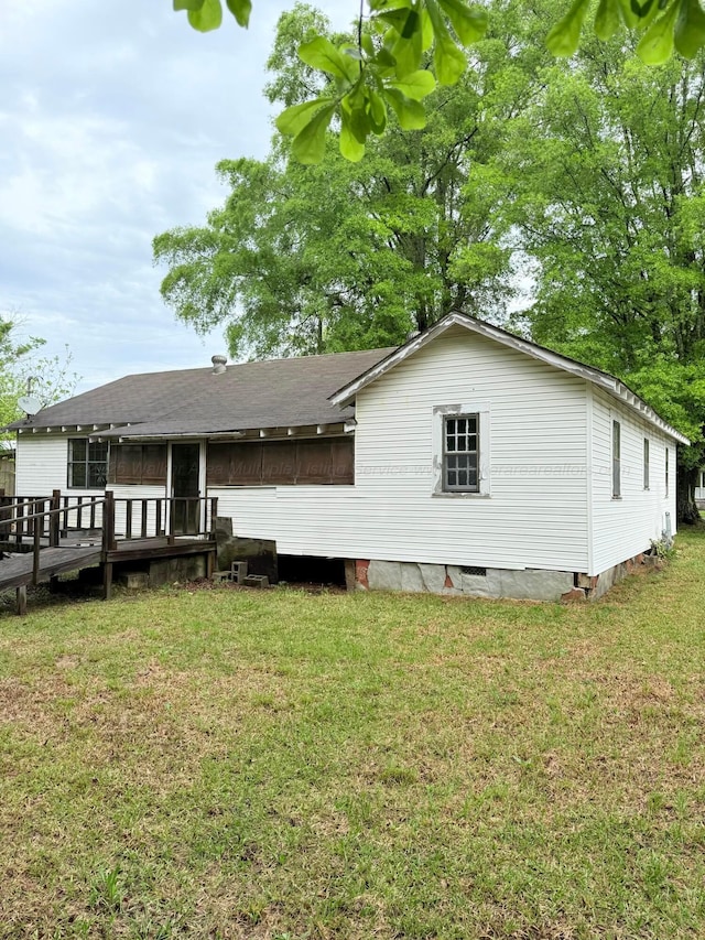 rear view of property featuring a lawn, a deck, and a shingled roof
