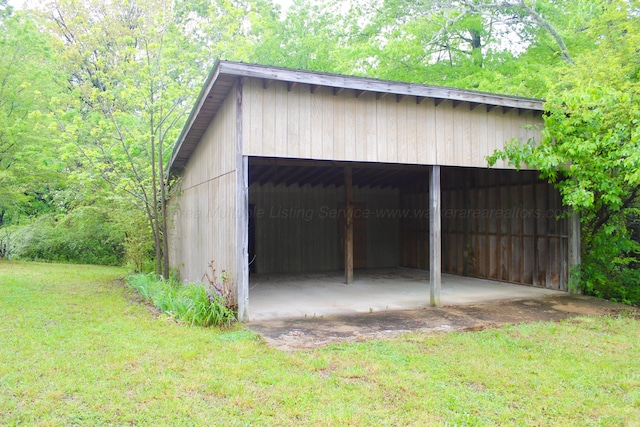 view of pole building with a detached carport, a lawn, and a wooded view