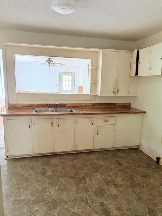 kitchen featuring open shelves, a textured ceiling, cream cabinetry, and a sink