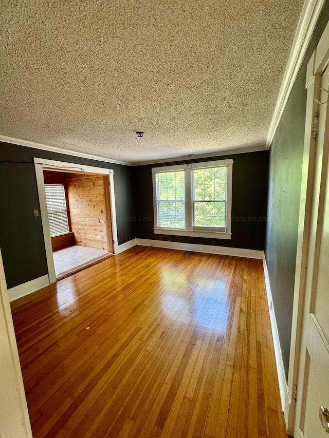 unfurnished room with hardwood / wood-style floors, a textured ceiling, baseboards, and crown molding