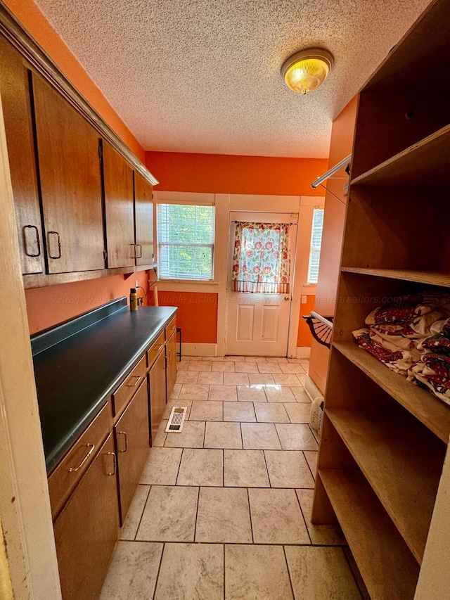 interior space featuring a textured ceiling, dark countertops, open shelves, brown cabinetry, and light tile patterned floors