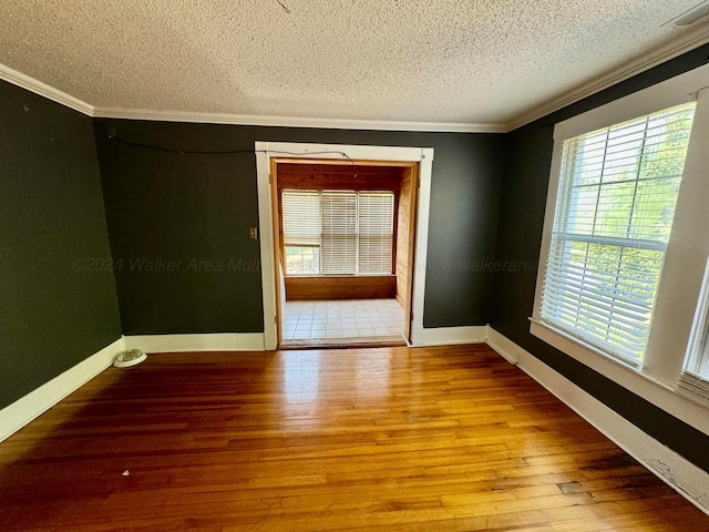 unfurnished room featuring baseboards, wood finished floors, ornamental molding, and a textured ceiling