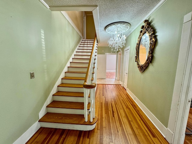 stairway featuring hardwood / wood-style floors, a textured ceiling, baseboards, and a chandelier