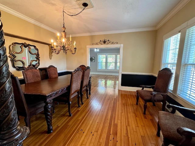 dining room featuring light wood-style flooring, ornamental molding, a chandelier, and a textured ceiling
