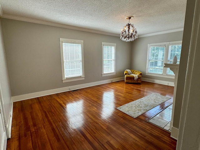 empty room featuring a textured ceiling, ornamental molding, a chandelier, and hardwood / wood-style flooring