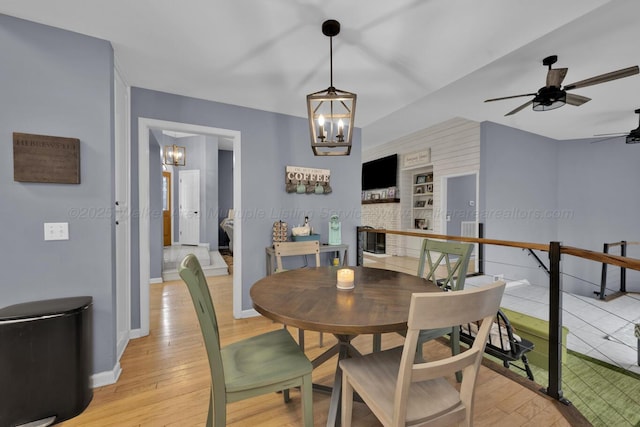 dining area with light wood finished floors, ceiling fan with notable chandelier, and baseboards