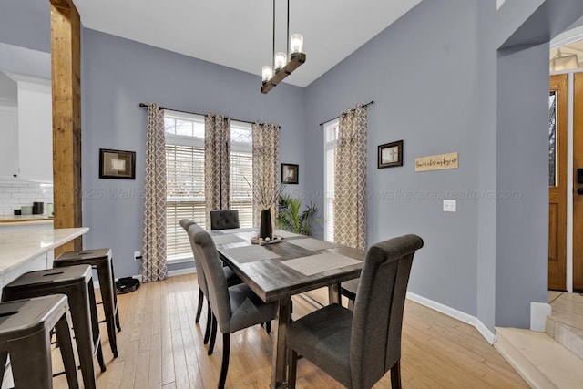 dining area with vaulted ceiling, a notable chandelier, light wood-style floors, and baseboards