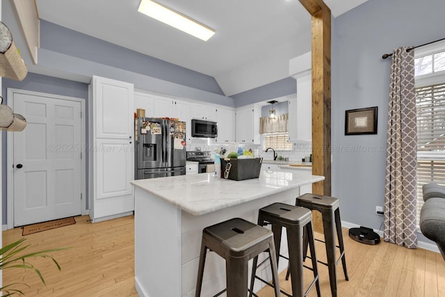 kitchen featuring vaulted ceiling, appliances with stainless steel finishes, light wood-style floors, white cabinetry, and a sink