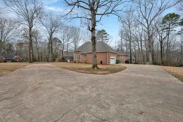 view of side of property featuring brick siding, concrete driveway, an attached garage, and a shingled roof