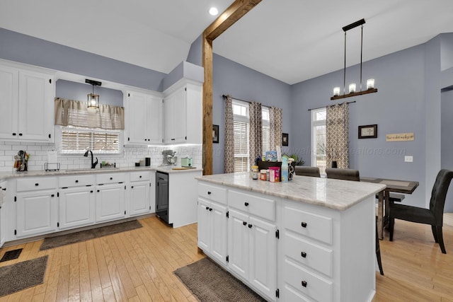 kitchen with light wood-style flooring, a sink, black dishwasher, a center island, and decorative backsplash