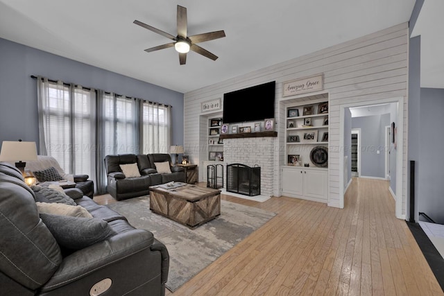 living room with a ceiling fan, a fireplace, and light wood finished floors