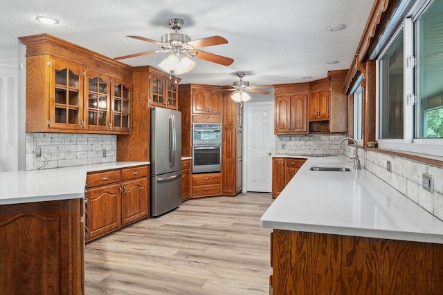 kitchen with backsplash, sink, ceiling fan, light hardwood / wood-style floors, and stainless steel appliances