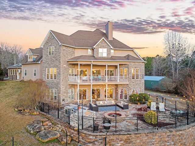 back house at dusk featuring a patio, a balcony, and an outdoor living space with a fire pit