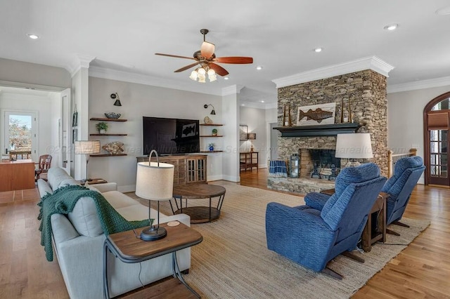 living room featuring baseboards, a stone fireplace, wood finished floors, and ornamental molding