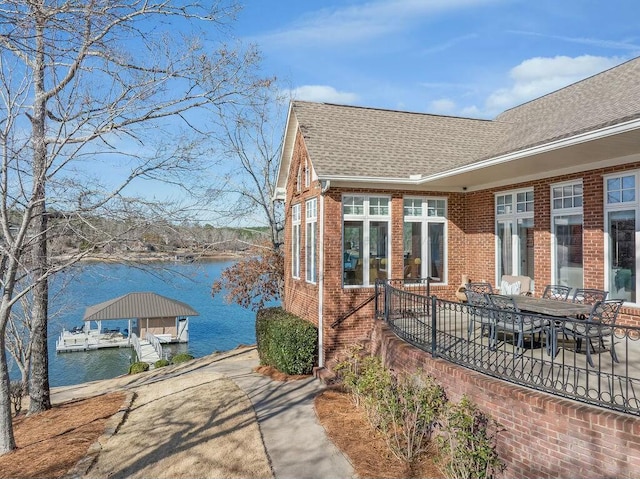 view of home's exterior featuring brick siding, roof with shingles, a boat dock, and a water view