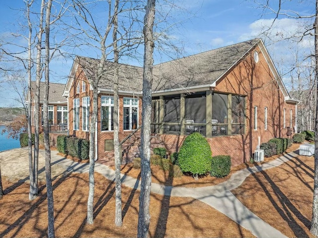 view of front facade featuring brick siding, a shingled roof, and a sunroom