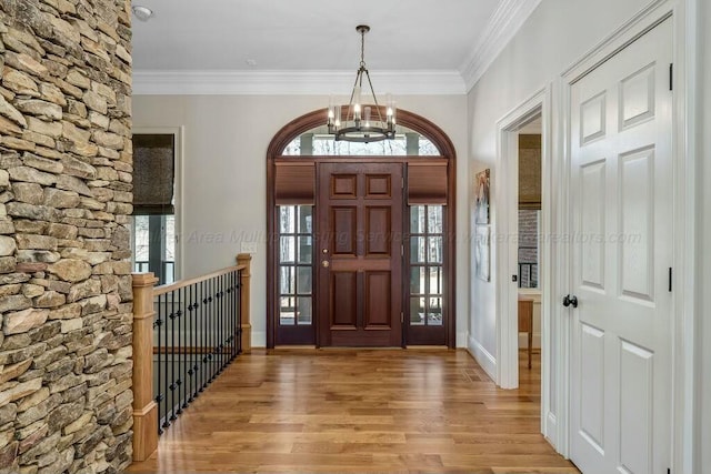 foyer featuring crown molding, light wood-style flooring, a healthy amount of sunlight, and a chandelier