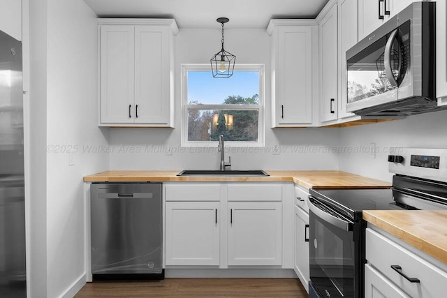 kitchen with wooden counters, stainless steel appliances, sink, decorative light fixtures, and white cabinetry