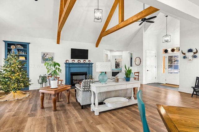 living room with built in shelves, hardwood / wood-style floors, ceiling fan with notable chandelier, high vaulted ceiling, and beamed ceiling