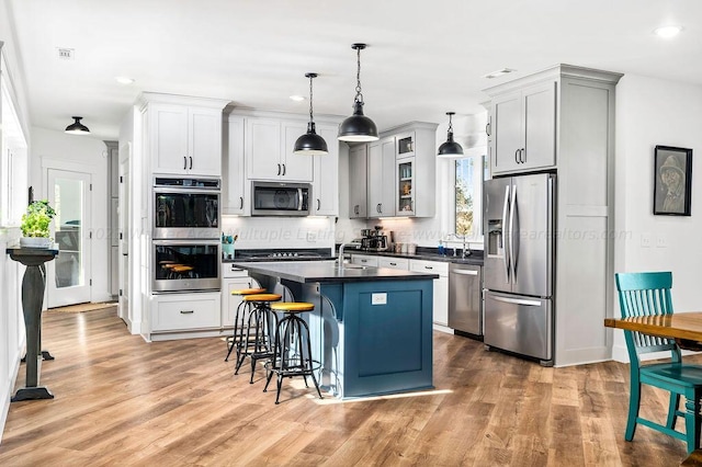 kitchen featuring appliances with stainless steel finishes, hanging light fixtures, light wood-type flooring, a center island with sink, and a breakfast bar area