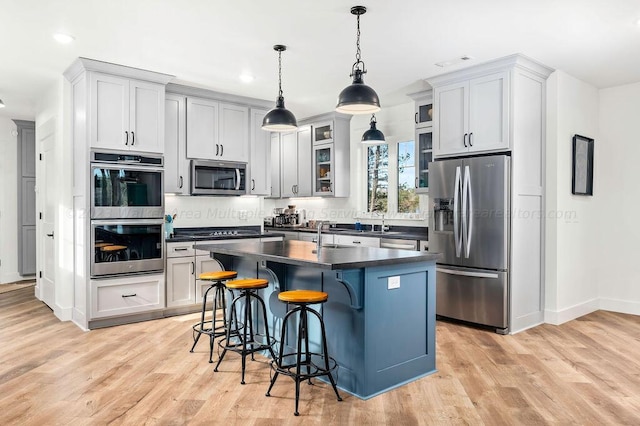 kitchen featuring appliances with stainless steel finishes, decorative light fixtures, light wood-type flooring, a kitchen island, and a breakfast bar area