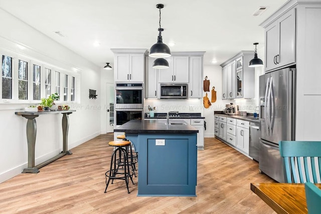 kitchen featuring decorative light fixtures, a breakfast bar, appliances with stainless steel finishes, and an island with sink