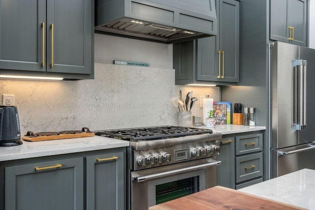 kitchen featuring backsplash, gray cabinets, custom exhaust hood, premium appliances, and light stone counters