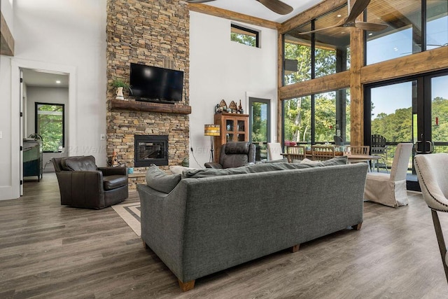 living room with ceiling fan, a fireplace, beam ceiling, a towering ceiling, and dark wood-type flooring