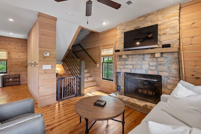 living room featuring wood walls, ceiling fan, light hardwood / wood-style floors, and a stone fireplace