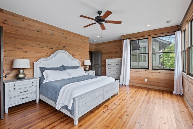 bedroom with ceiling fan, wood walls, and light wood-type flooring