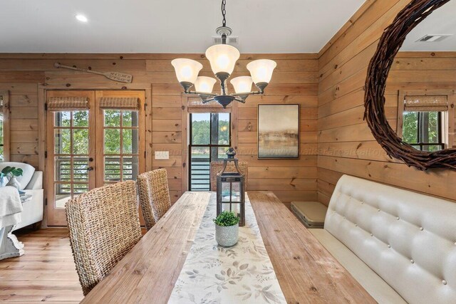 dining area with a chandelier, wooden walls, wood-type flooring, and french doors