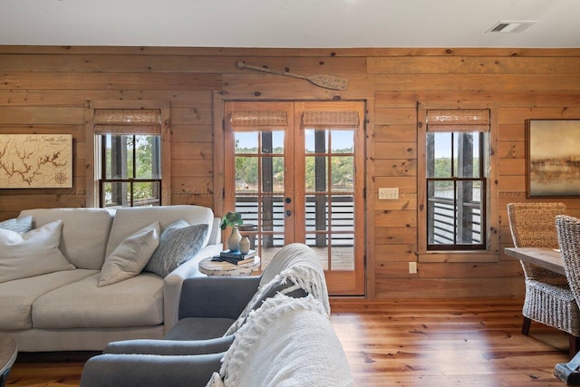 living room with wood walls, wood-type flooring, a wealth of natural light, and french doors