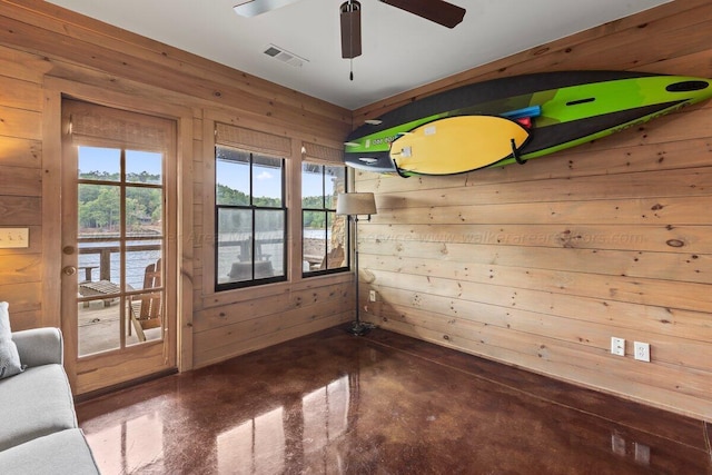 unfurnished room with a water view, ceiling fan, and wood walls