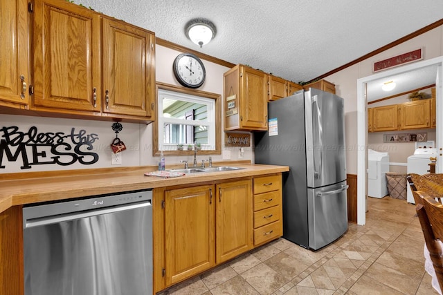 kitchen with sink, ornamental molding, a textured ceiling, appliances with stainless steel finishes, and washing machine and clothes dryer