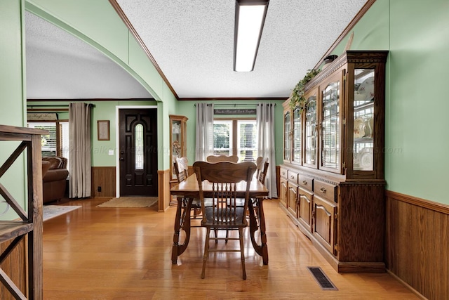 dining space featuring wood walls, light hardwood / wood-style floors, crown molding, and a textured ceiling