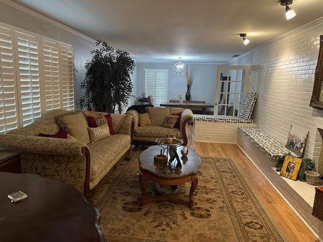 living room featuring a chandelier, ornamental molding, brick wall, and hardwood / wood-style flooring