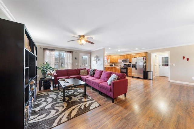 living area with light wood-style floors, baseboards, ornamental molding, and a ceiling fan