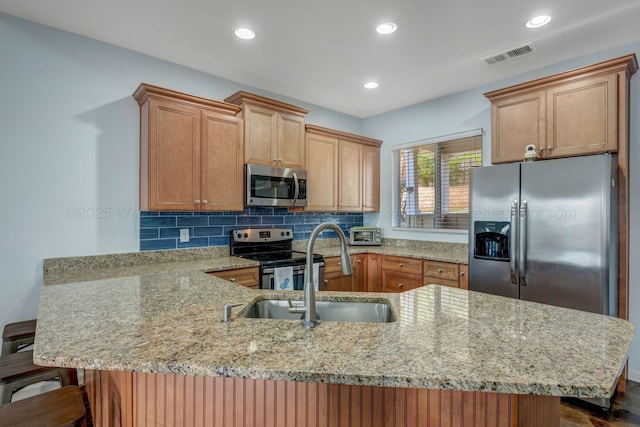 kitchen featuring a kitchen bar, sink, light stone counters, stainless steel appliances, and backsplash